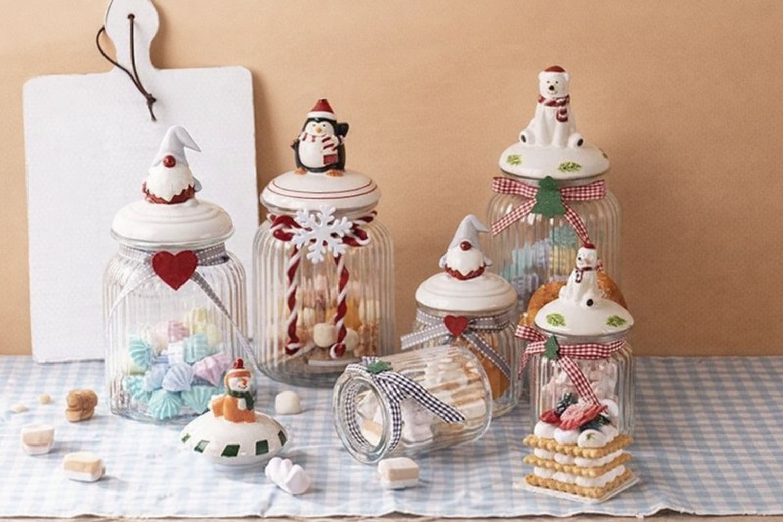 Julpyntade burkar med godis och bakverk på ett rutigt bord, mot en beige vägg.