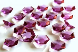 Många lila glittrande "diamanter" av isomalt utspridda på en vit yta.
