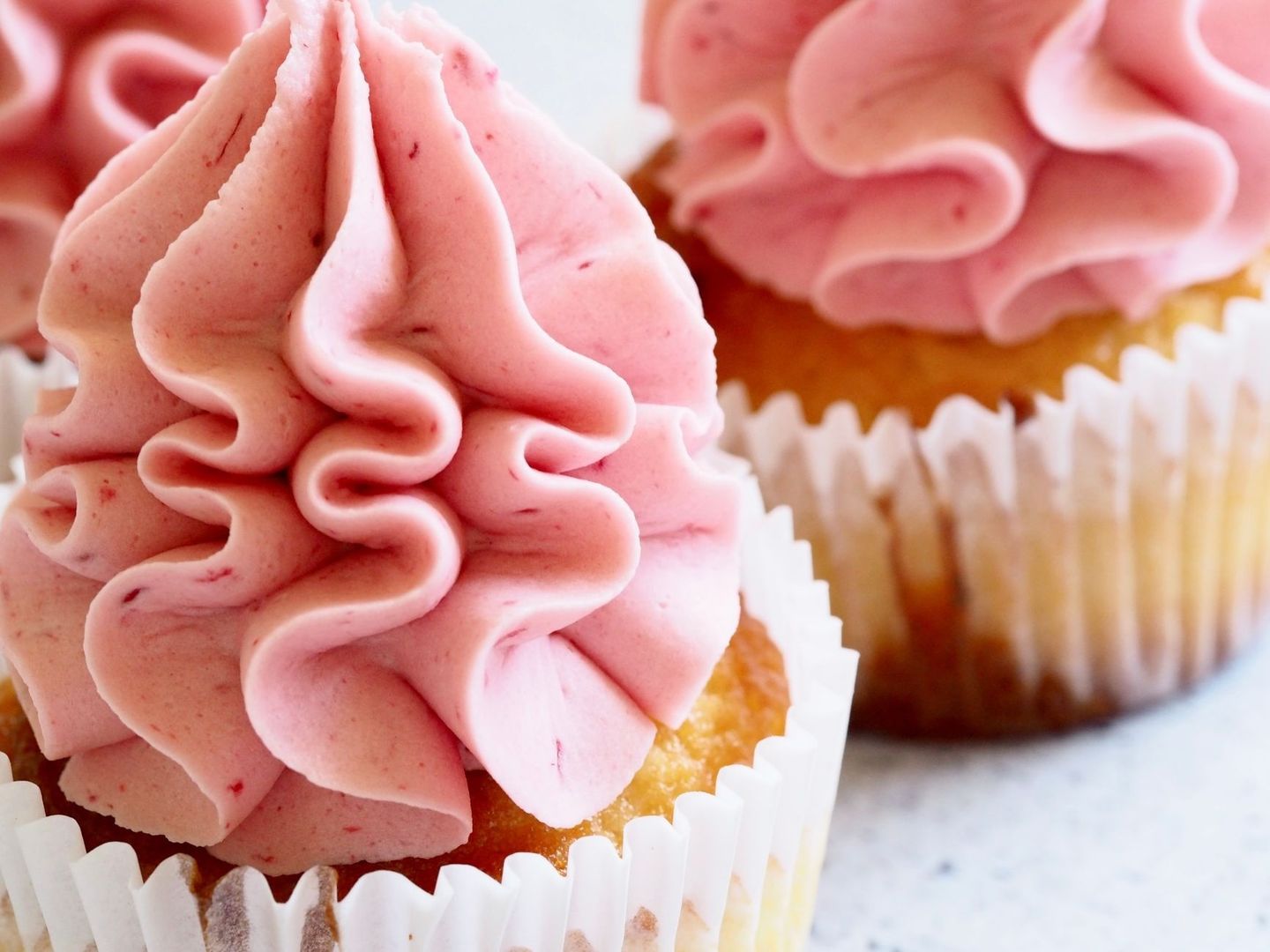 Rosa, slät smörkräm spritsad i mjuka virvlar på cupcakes